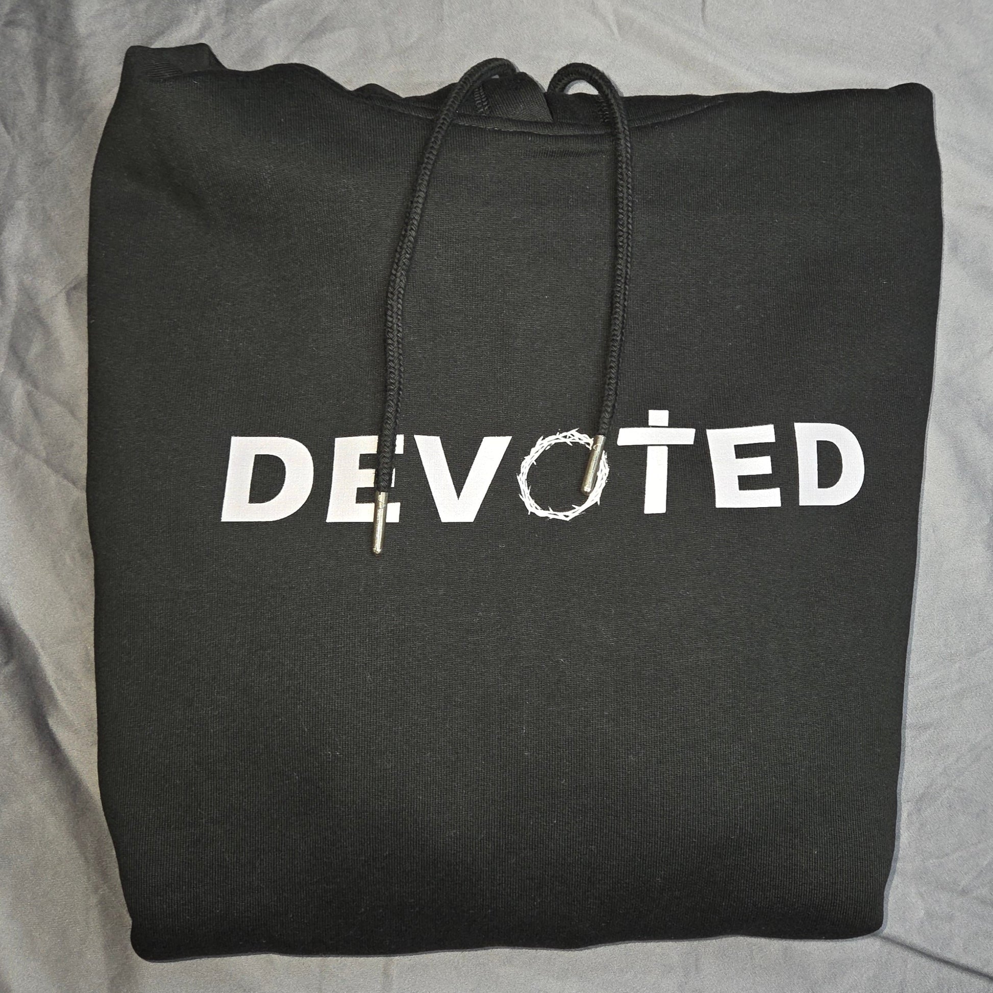 Black hoodie with 'DEVOTED' printed on it, folded on a gray surface